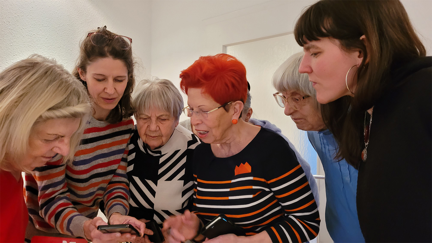 Die Trainerin Stefanie Schaarschmidt zeigt vier Teilnehmerinnen einer Lerngruppe etwas am Smartphone.